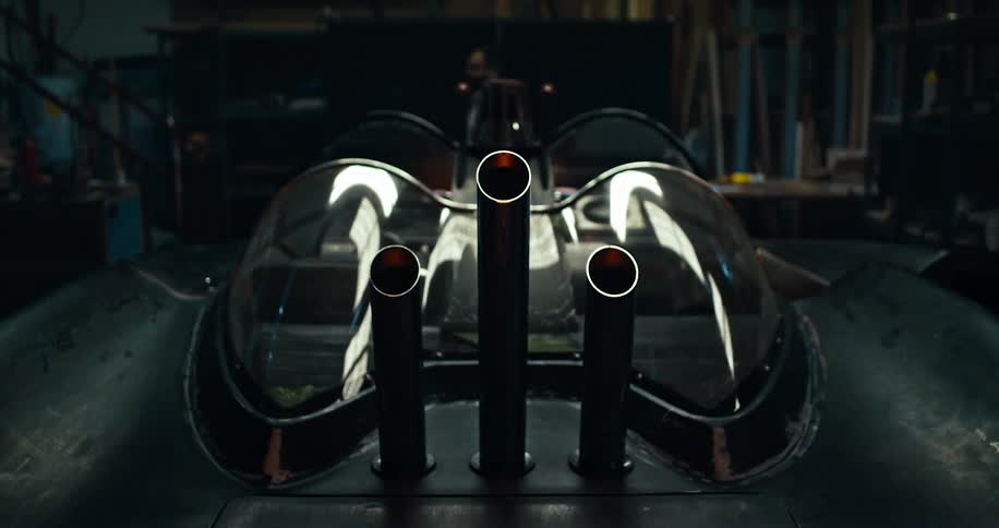 Man walks across garage passing car with three exhausts and glass cockpit