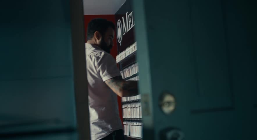 A shopkeeper seen through a doorway as he places products on the shelf of his shop