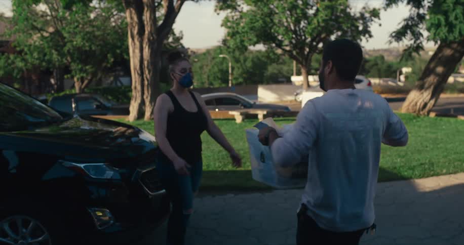 A man carries a large plastic bin full of clothes out of his garage and hands it to a woman
