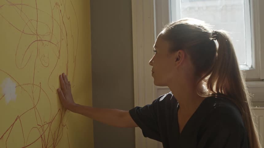 Woman crouches near window touching flat yellow surface with drawing