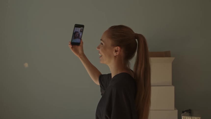 A woman stands inside of a home on her phone video chatting with a male friend appearing to show off her new home