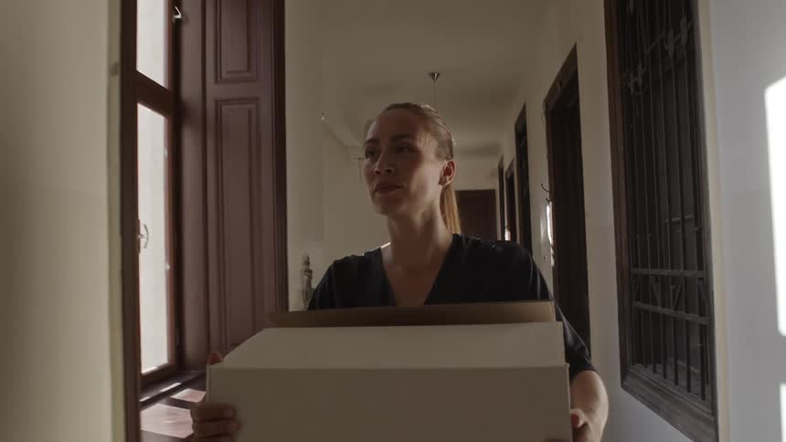 Woman walking down a hallway in an apartment building holding a moving box
