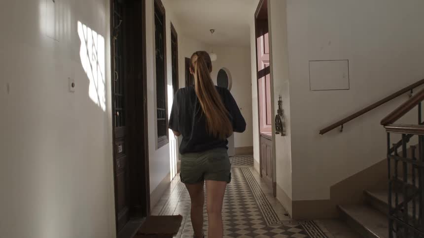 A young woman carries a moving box down a hallway in an apartment building