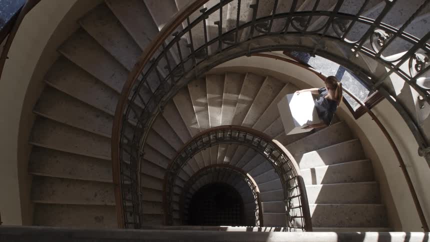 A woman carrying a box down a spiral staircase