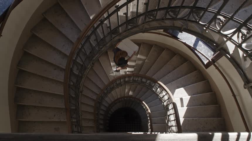 A woman walks up a spiral staircase while holding a white box