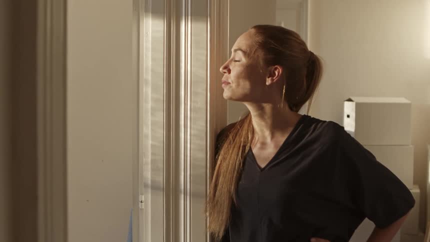 A woman puts her hands to her hips and exhales as she looks out of a room