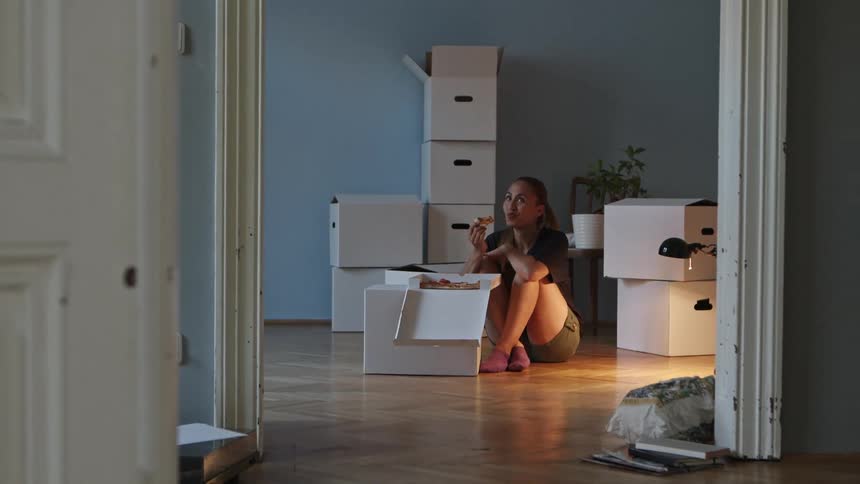 A woman sitting on the floor in a room eating pizza out of the box