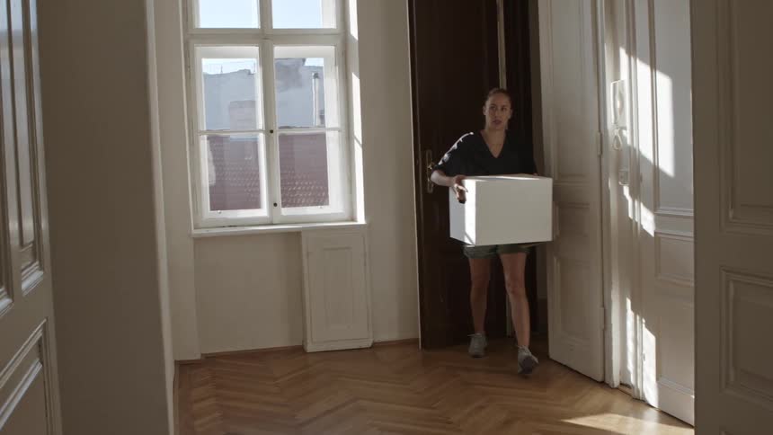 A woman carries a cardboard box into her new apartment