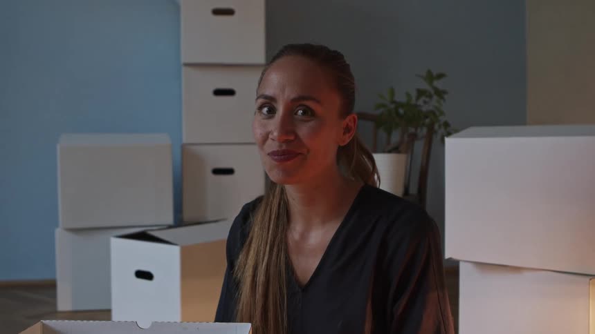 A woman sits in a house surrounded by moving boxes