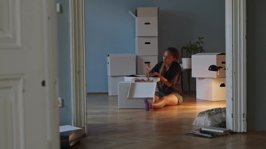 A woman sitting on the floor in a room eating pizza out of the box