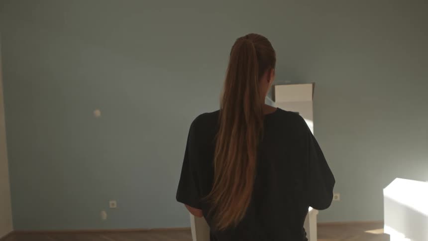 A young woman carries a moving box in the hallway of a home
