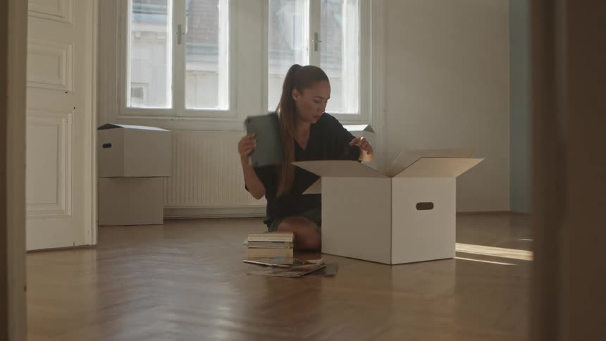 A woman sitting on the floor in a room putting books into a box