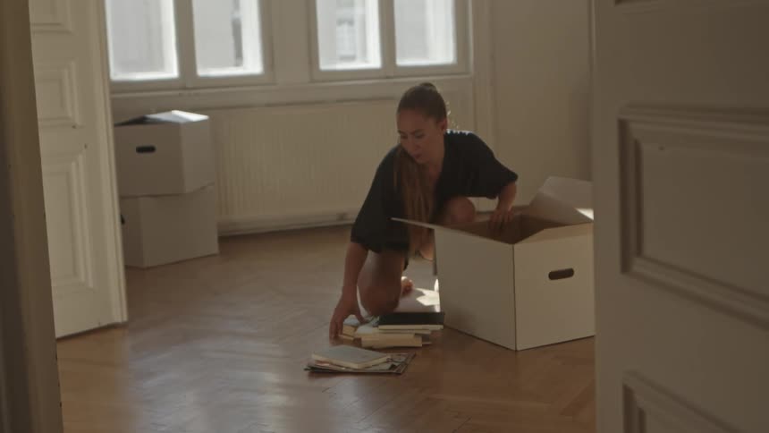 A woman is kneeling on the floor while placing books into a box