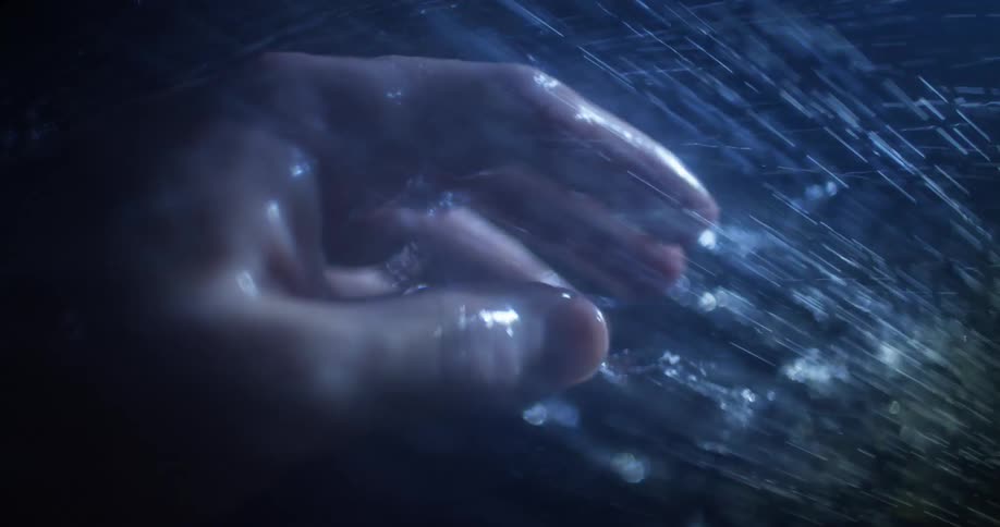 Stream of water droplets rush over a wet human hand in the dark