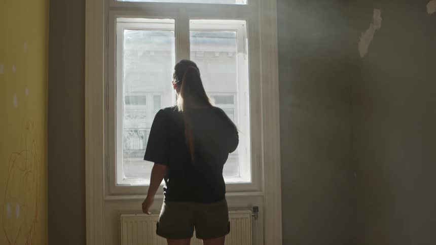 A female walks up to a set of windows and opens them