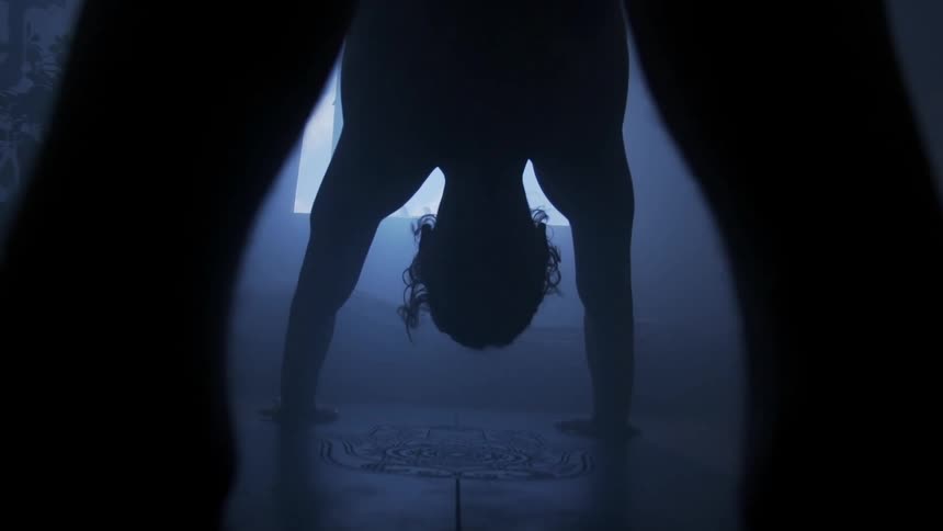 Sunlight shines through a window into a dark room where a man is holding a yoga pose