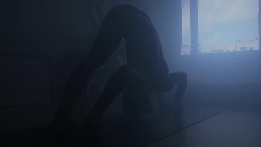 A man takes a yoga pose on a yoga mat in a dimly lit room during the day