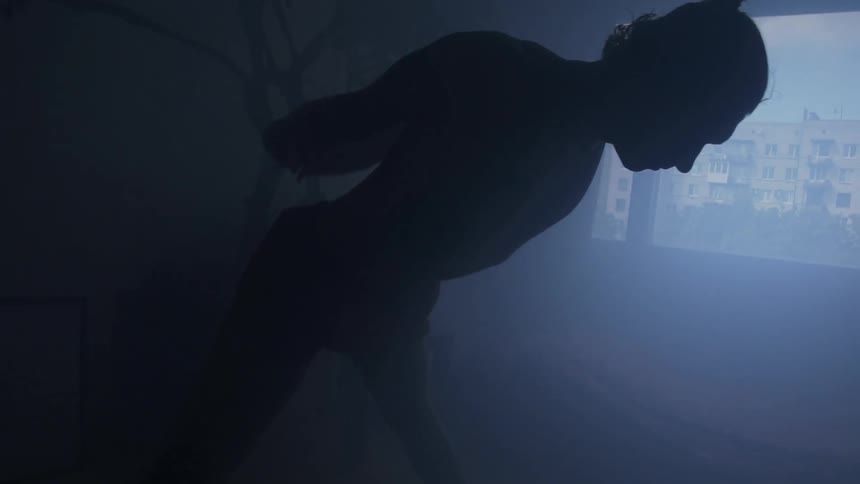 A shadowy man in a misty room stretches and performs yoga in his home
