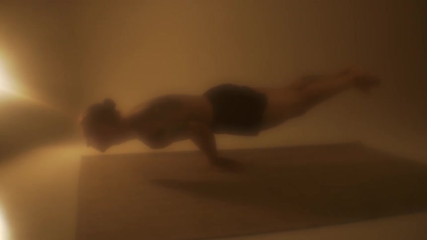 A shirtless man holds a yoga hand stand on a yoga mat in an enclosed room