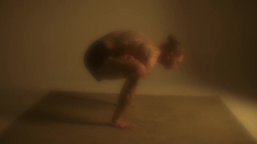 A man with tattoos standing on his hands on a mat in a room