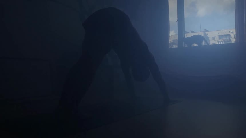 A man does yoga on a yoga mat in a dark room on a sunny day