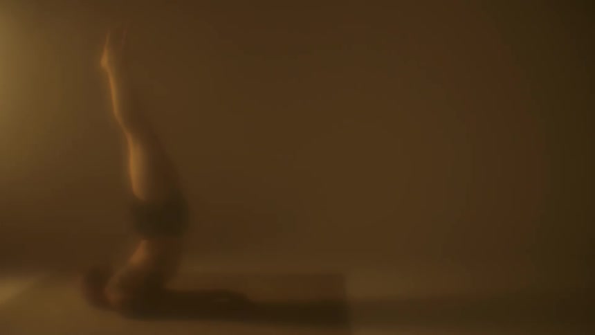 A man in his underwear holds a difficult yoga pose in a dimly lit room