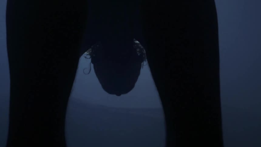 A person is bent over supporting with arms and leaps forward landing on feet in front of a window in a dark room