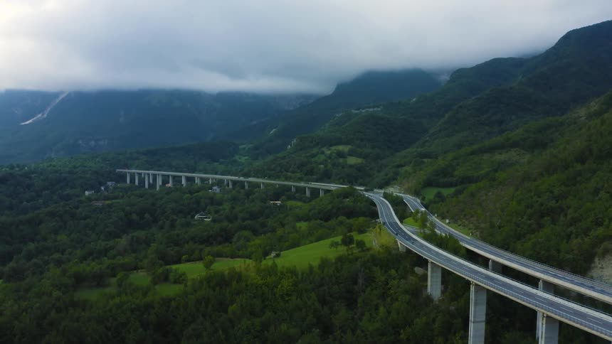 A long freeway bridge through a mountain valley under a sky of thick clouds