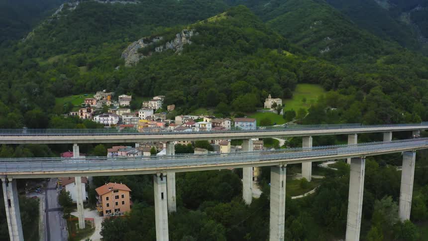 A truck drives by on a highway overpass where a small town sits underneath surrounded by greenery and trees