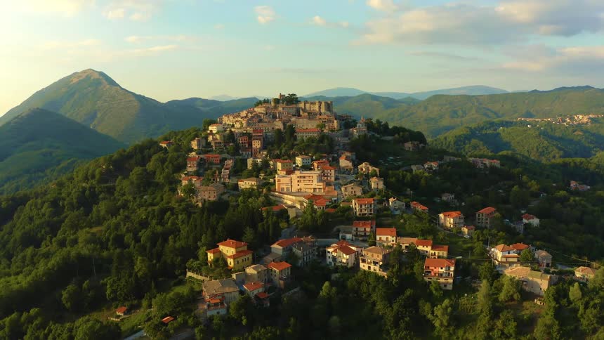 A town located on the slope and summit of a mountain covered in forest during golden hour