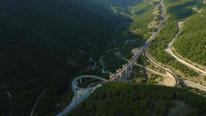 Mountains with roads intersecting with trees green sunlight and mist in the background