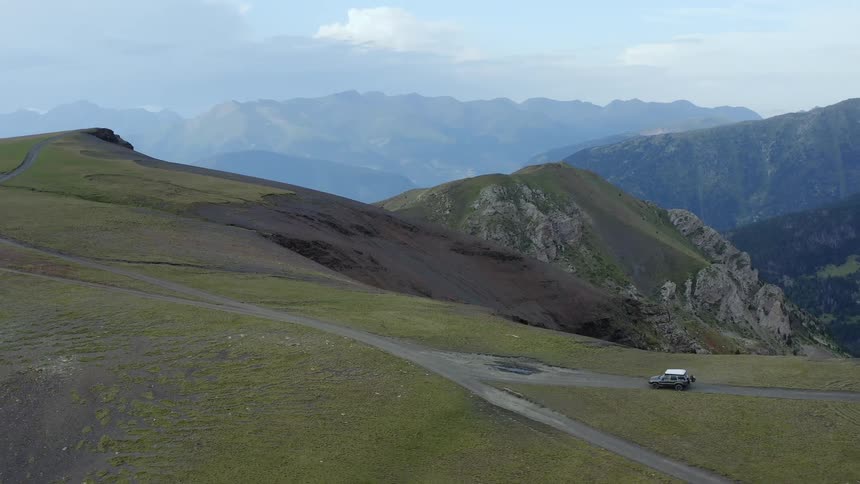 A vehicle driving on a road on a hill with a mountain range the sky and clouds in the background