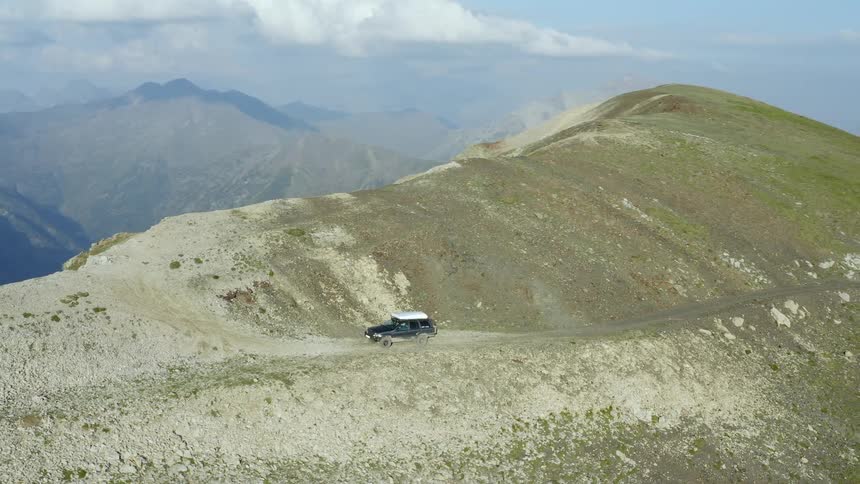 A jeep is sitting on the side of a mountain with mountain range all around on a sunny day