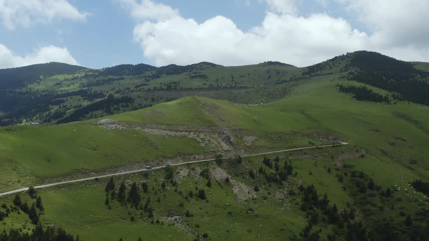 A vehicle travels along a road high in the hills in the countryside on a sunny day