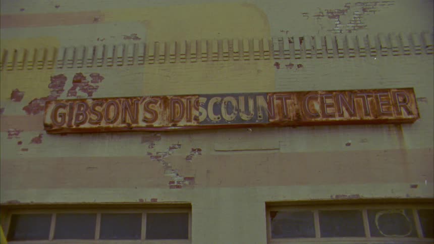 An old building with some of its paint missing is shown with a dilapidated old sign to an old store thats covered in rust