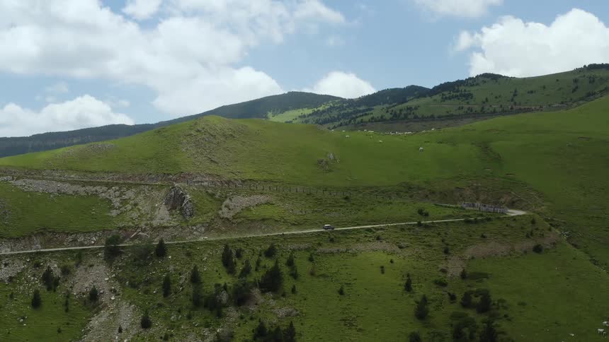 A vehicle driving on a road with hills the sky and clouds in the background