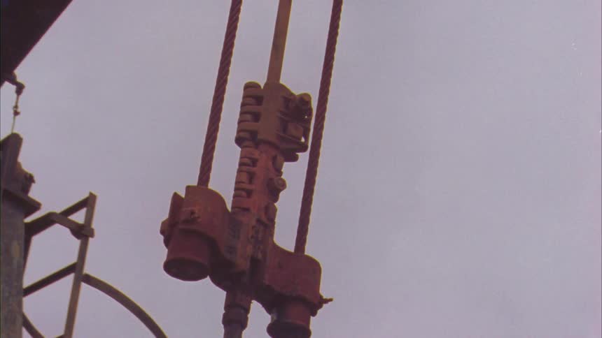 A large zoomed in piece of rusty street equipment hangs above some trees on a cloudy day