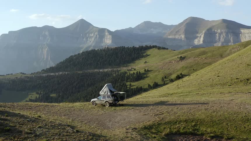A tent erected on the roof of a vehicle in a hilly countryside on a sunny day