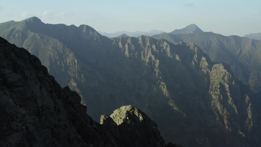 A car sits parked on top of a mountain trail in the morning with large mountains and a clear sky in the background