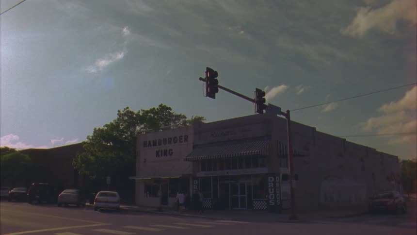 Small town with small businesses and parked cars while people walk on the sidewalks midday