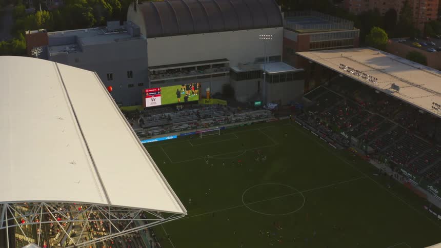A soccer stadium with players and fans and a big screen