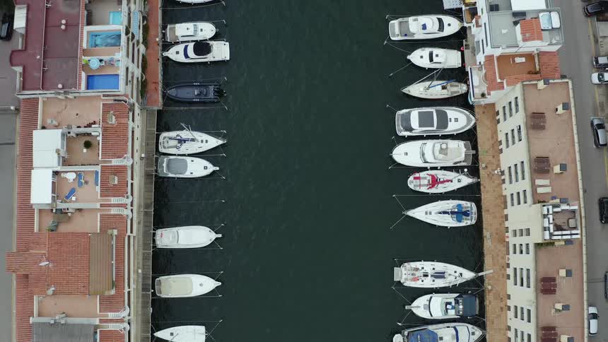 An aerial view of cars driving along a street on the shore with boats parked and sailing in the water