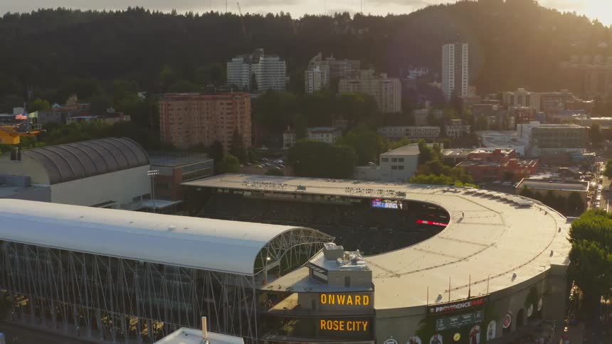 A camera zooms out of a stadium with cityscape and hills in the background