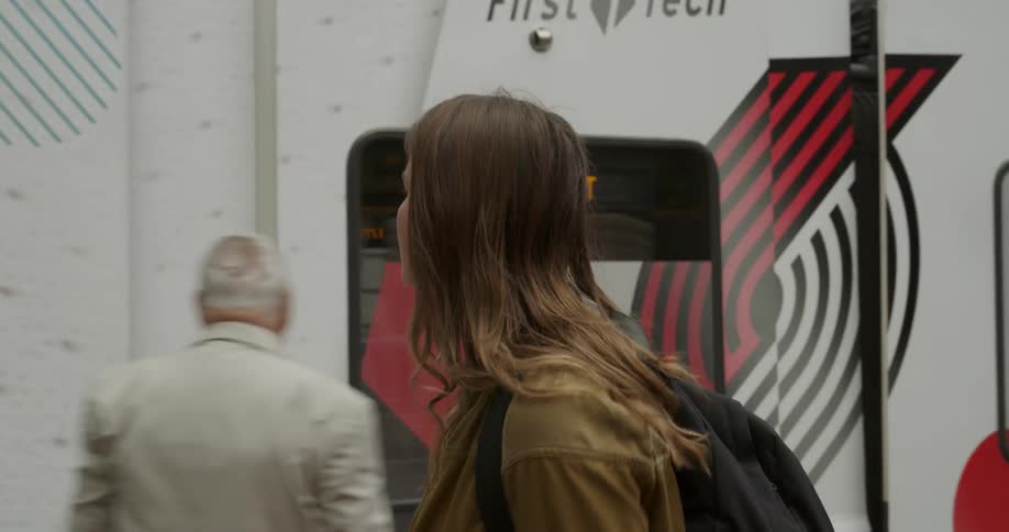 Woman walks along transit terminal watching train headed toward airport move by