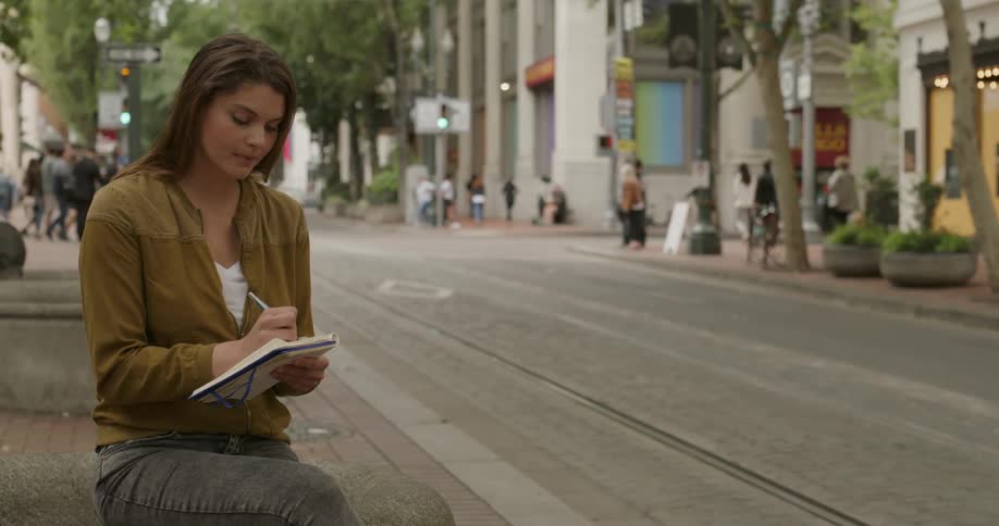 A woman stands on a city sidewalk writing in a notepad