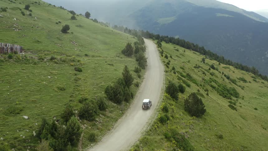 A car drives along a remote road in a mountain during the day with sun shining