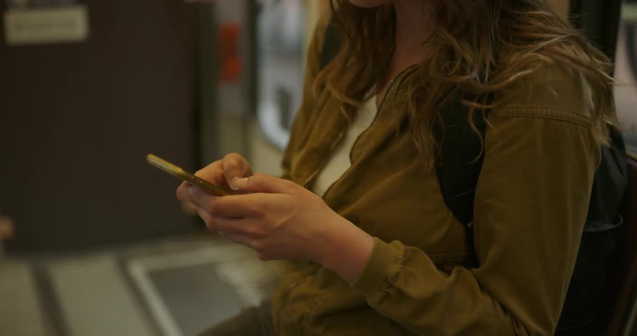 A teenage girl sits on a bus and uses her cell phone