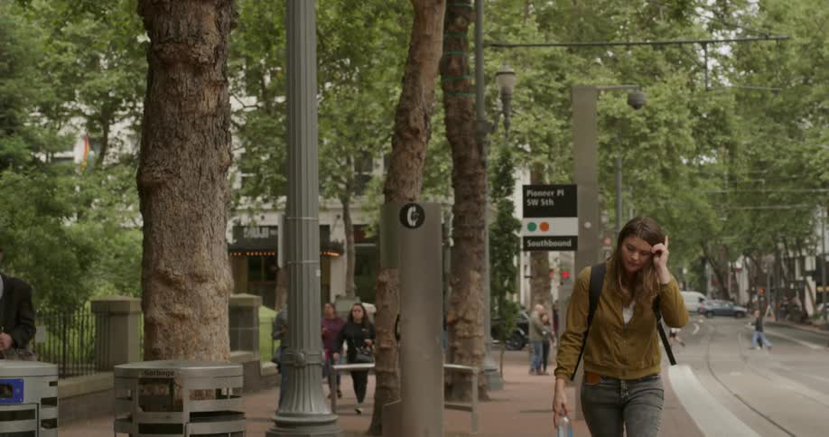 Woman walks past a city park while carrying a water bottle as other pedestrians walk nearby