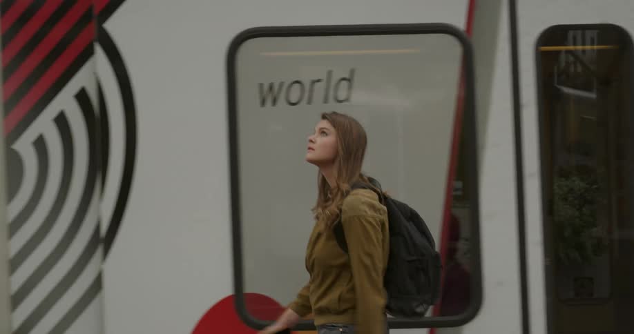A woman walks down a street pass a train looking around curiously with a backpack on