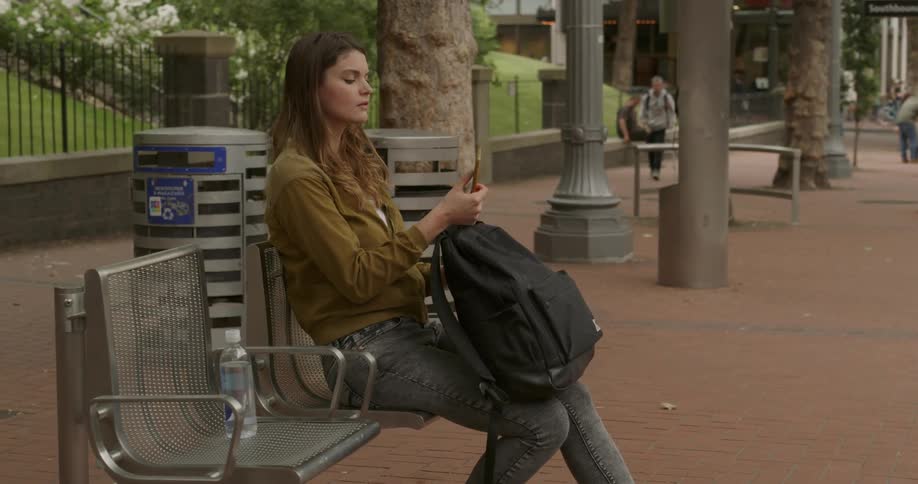 A woman with a smart phone and a backpack sitting on a bench